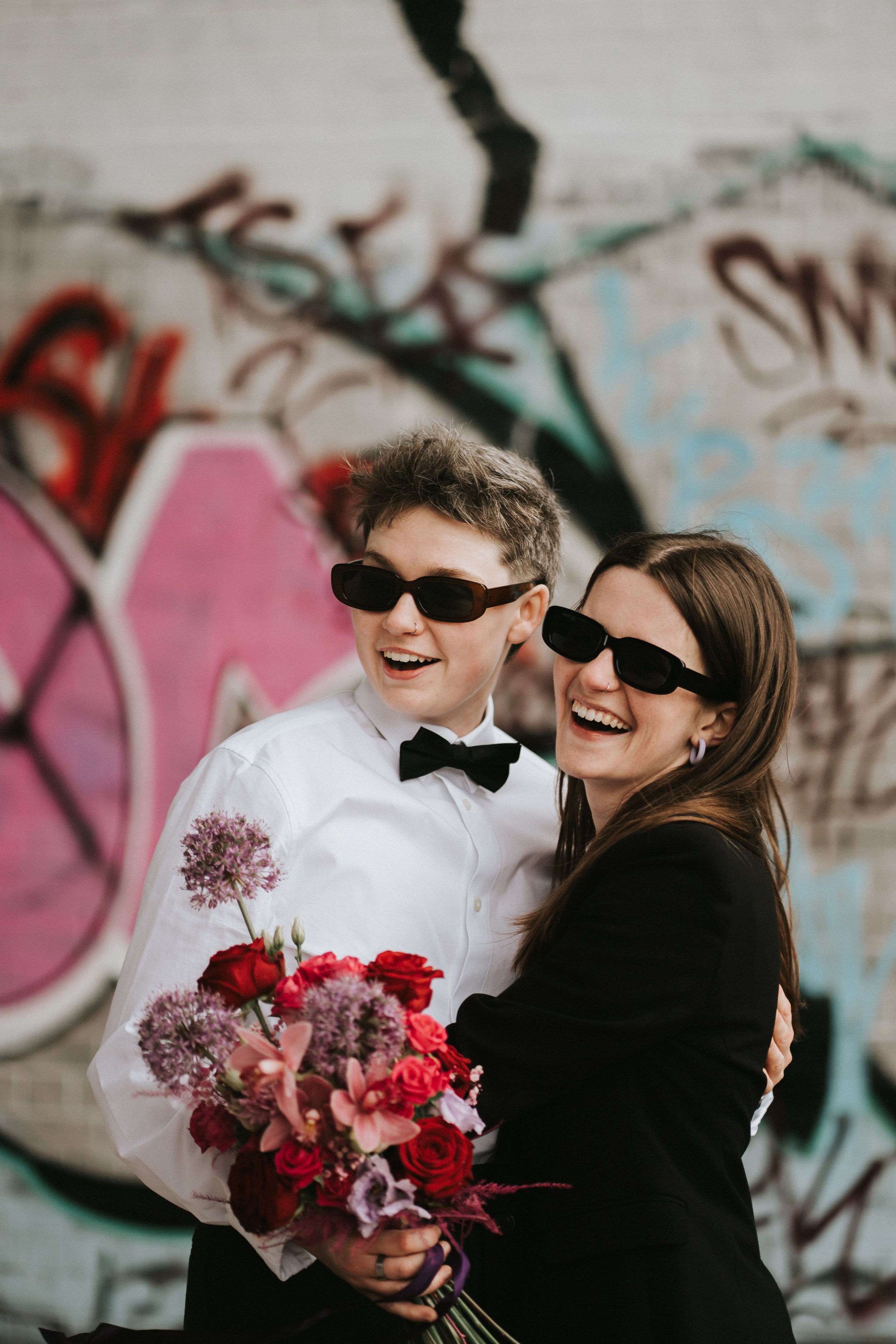 a couple after a city elopement in Digbeth Birmingham both wearing sunglasses and holding flowers
