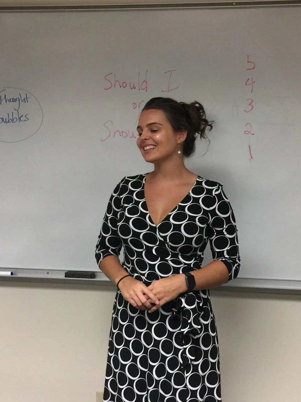 Brittany Evans in an updo and a black and white patterned dress standing in front of a whiteboard with writing in red and blue.