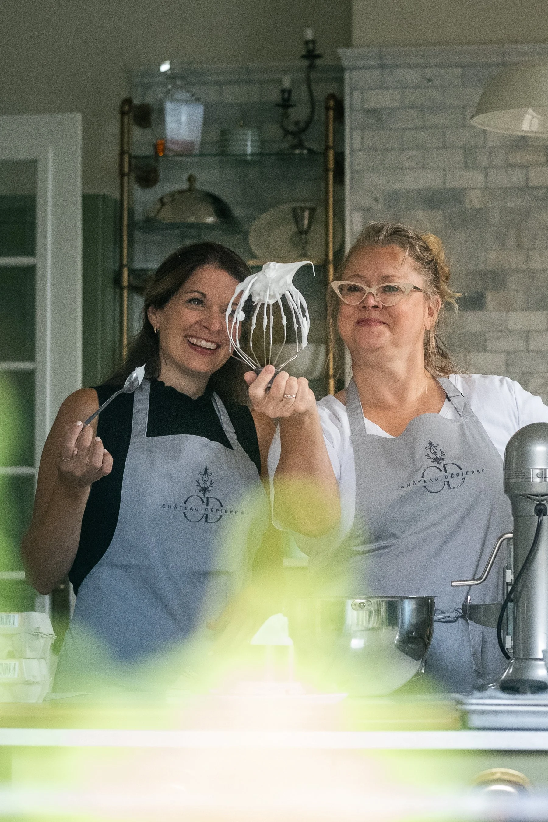 A bed with dark green pillows in a cozy bedroom with a painting on the green wall, a nightstand with a lamp, and curtains.