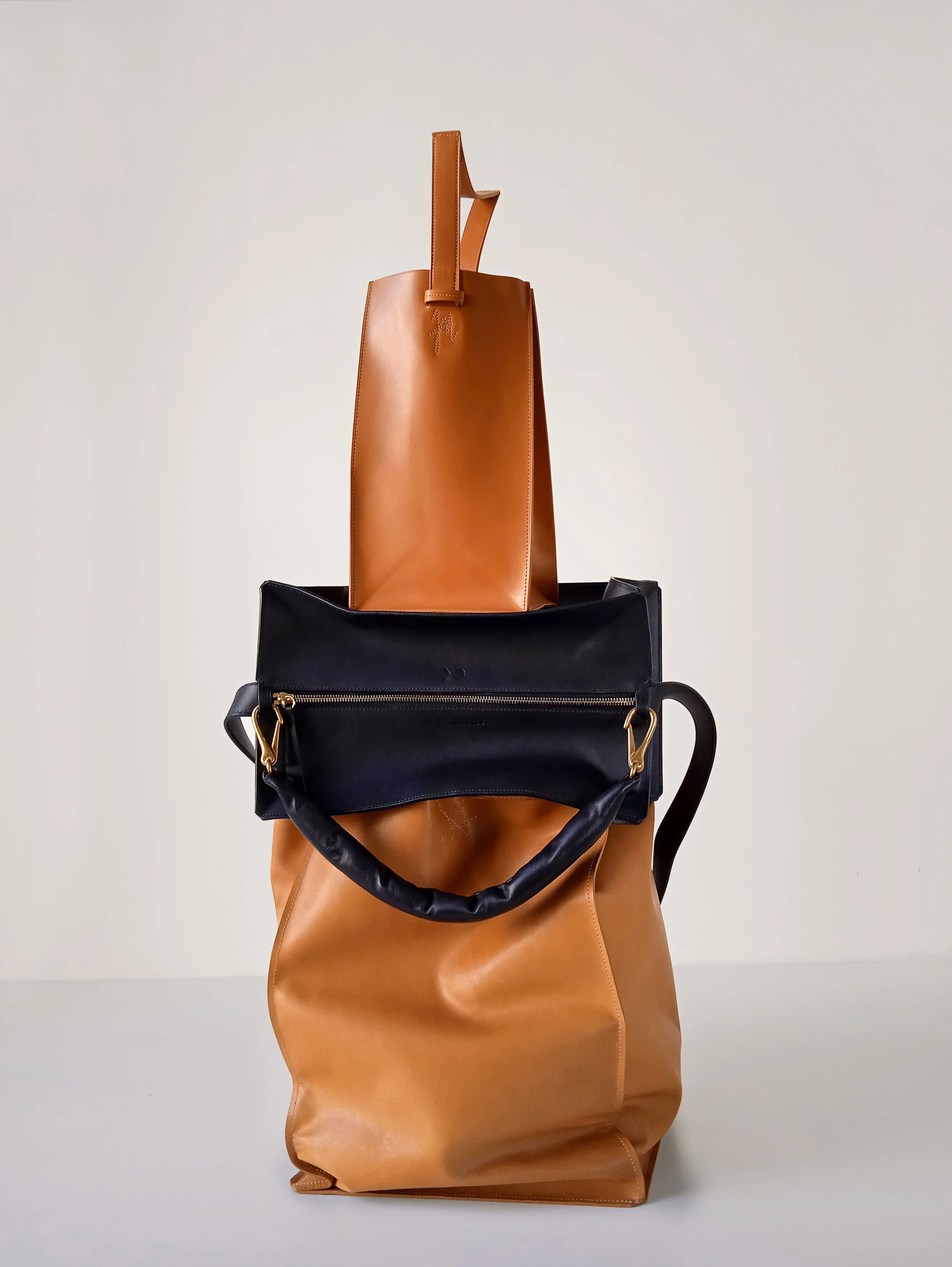 Three leather bags stacked, with a tan bag at the bottom, a black bag in the middle, and a smaller tan bag on top.