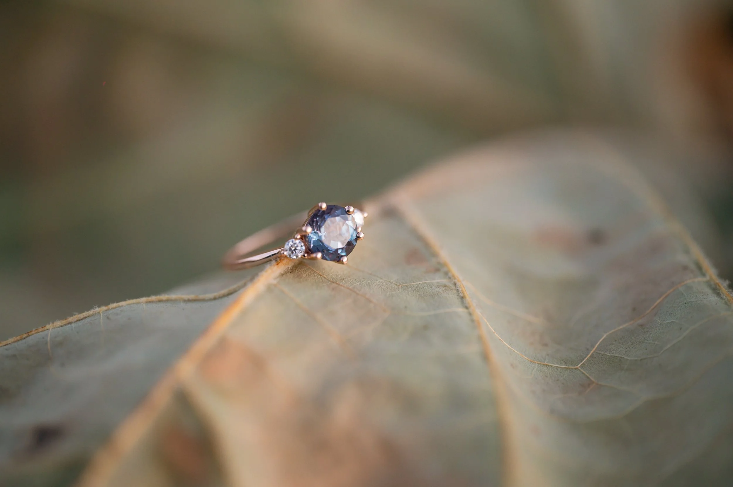 A purple stone ring on a rose gold band rests on a leaf.