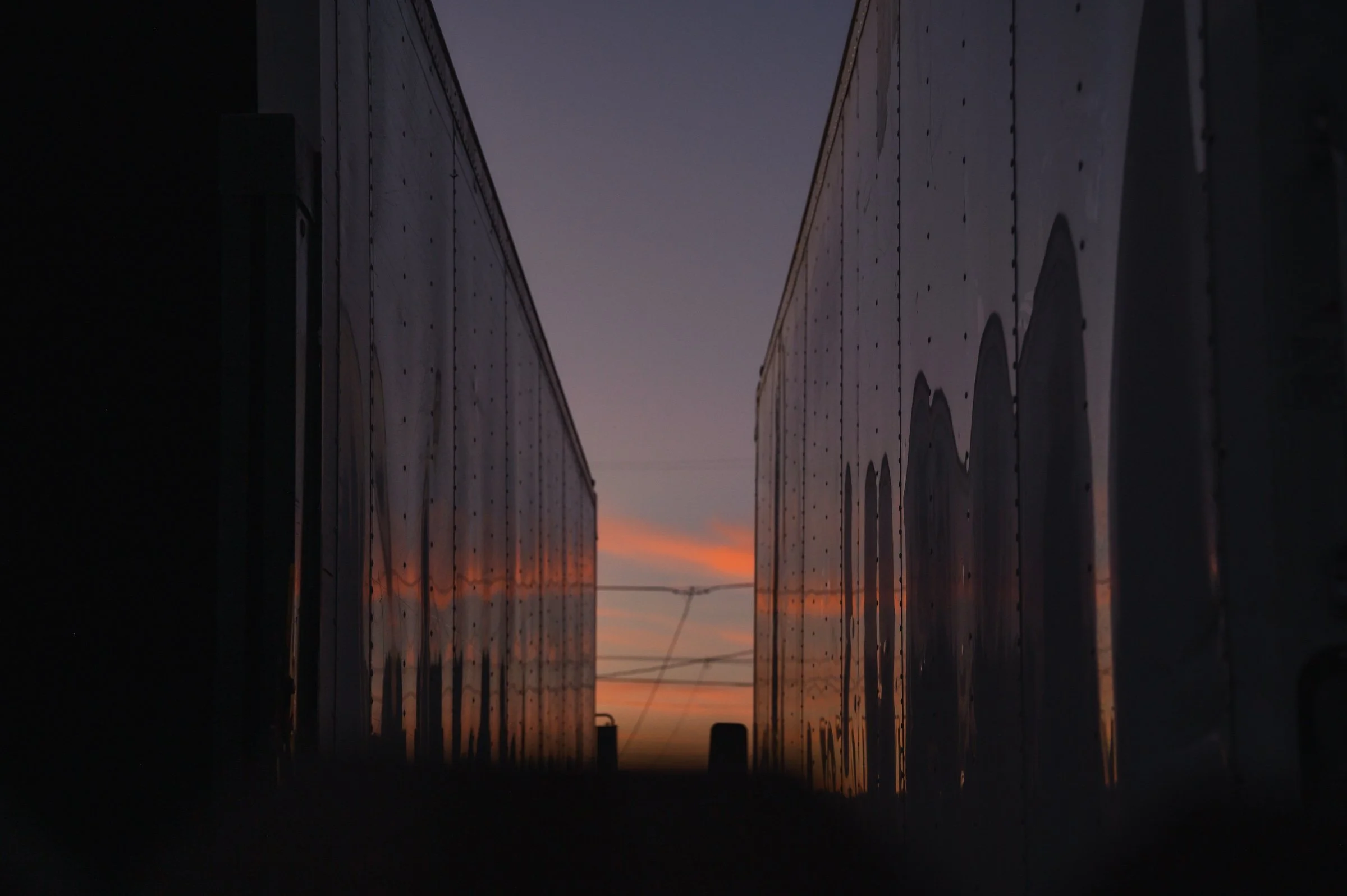 Two trains aligned parallel with sunset in the background.