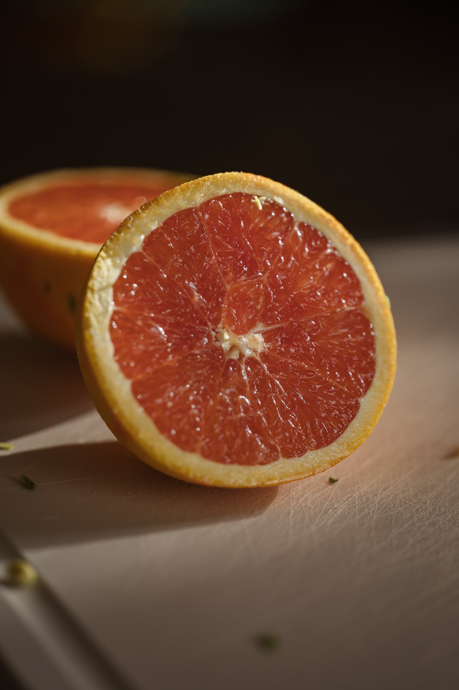 Close-up of a halved grapefruit with bright red flesh, placed on a wooden surface against a dark background.