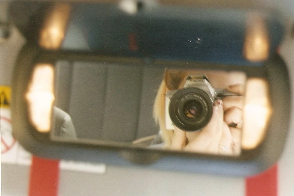 A person taking a photo of themselves in a car rearview mirror with a camera.