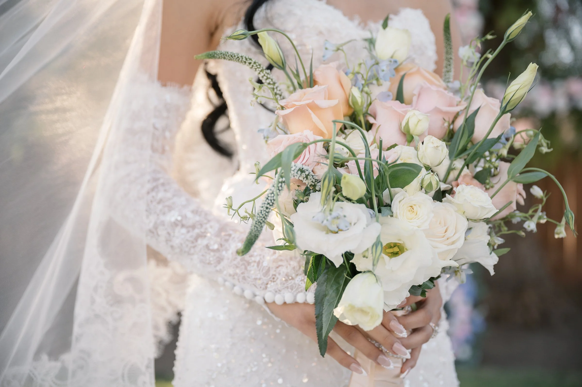 Bride holding a lush bouquet of pale pink and white roses with green foliage. She wears an elegant lace gown, conveying a romantic, serene mood.