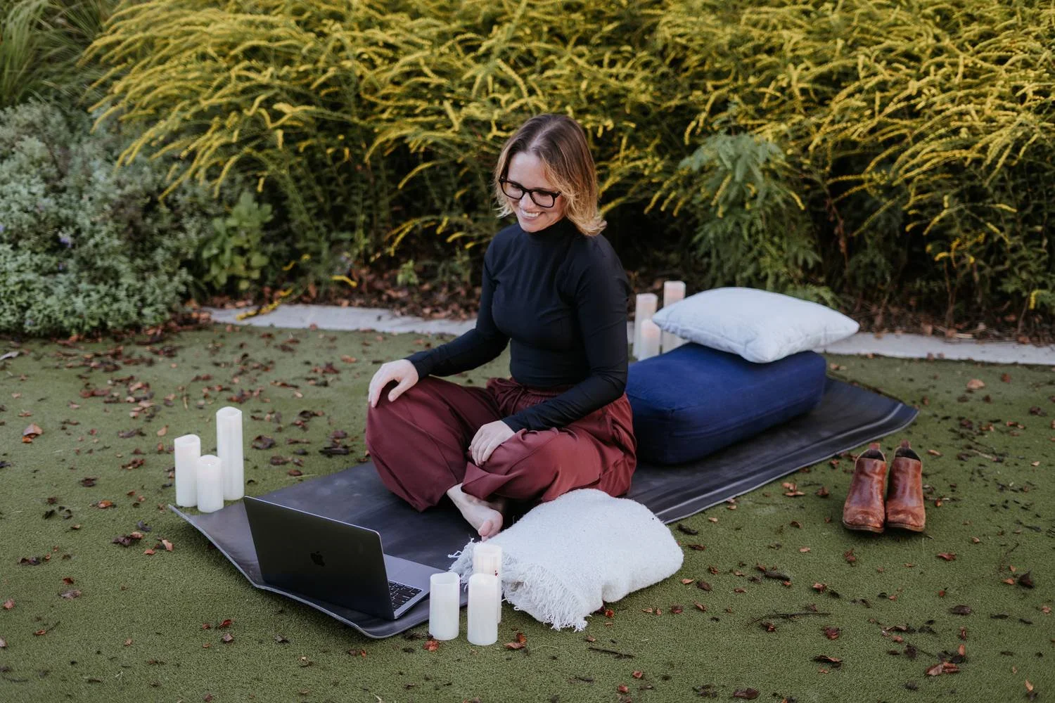 Amber Harris sitting cross-legged on a yoga mat outdoors with a laptop and candles, working with intention