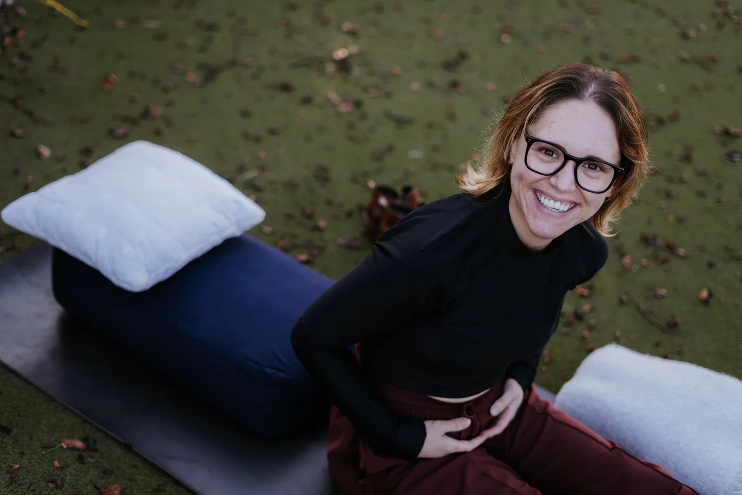 Amber Harris smiling up at the camera from her yoga mat, at ease and fully present