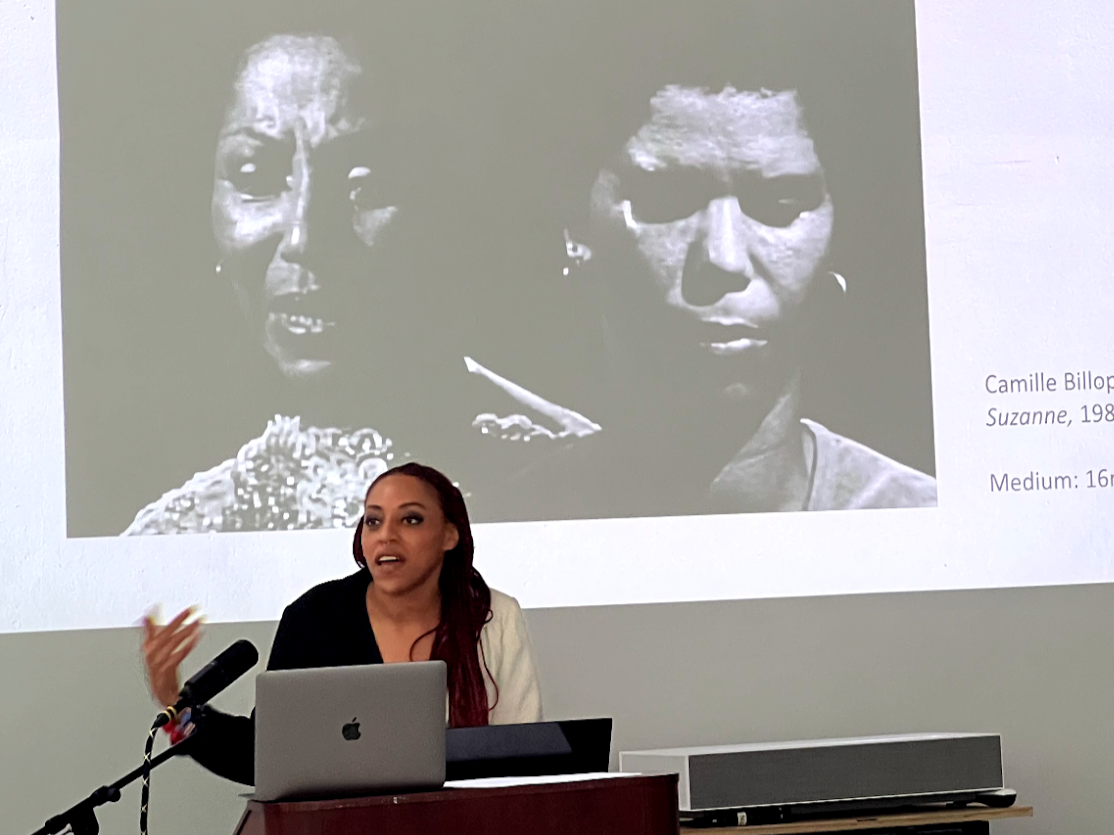 A photo of Ayana Dozier giving a tlak with a black and white image of two Black woman projected behind her