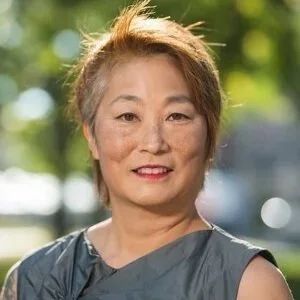 A photo of Lisa Nakamura, an East Asian woman with short hair and a gray blouse, smilling outdoors