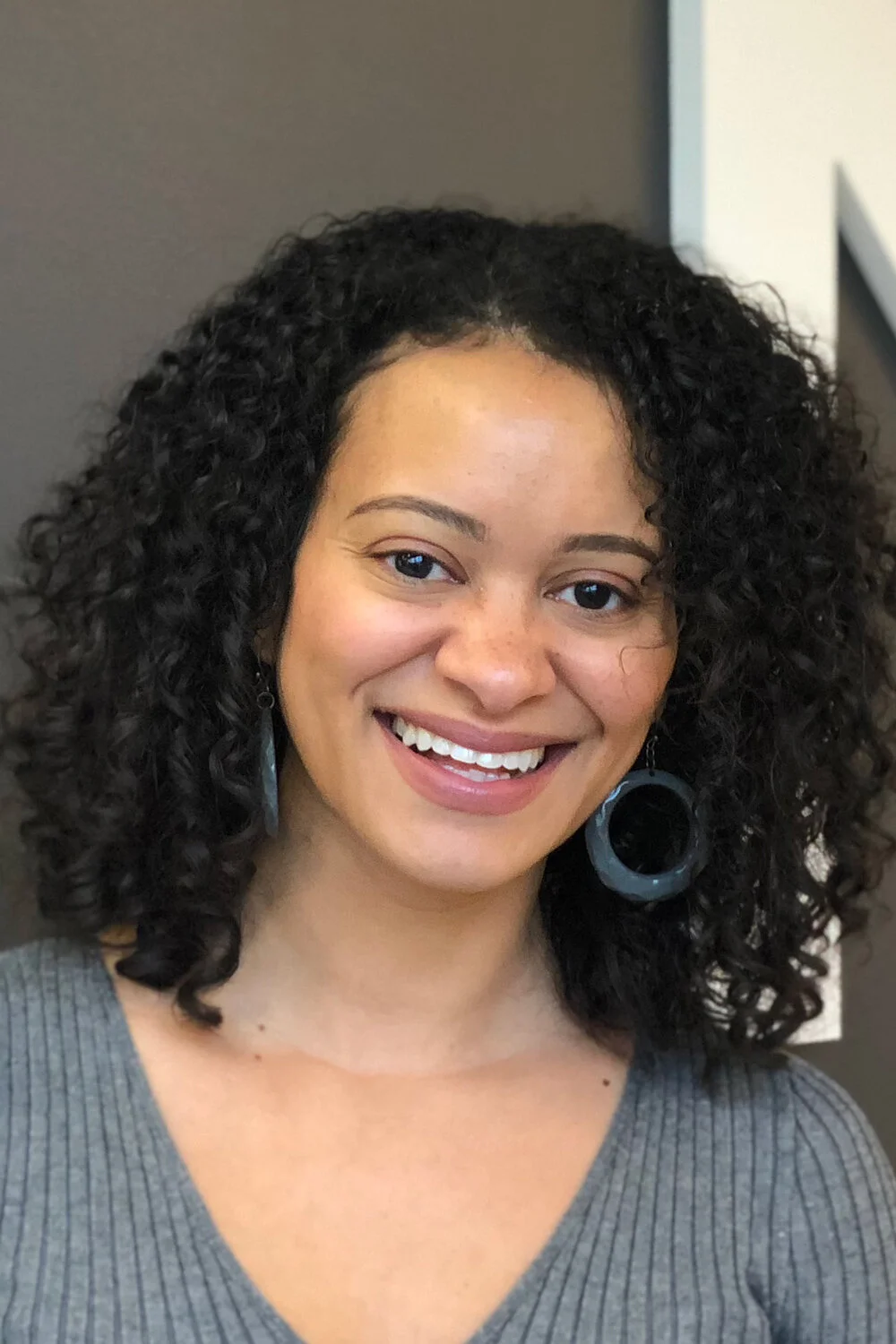 A photo of Catherine Knight Steele, a woman with dark curly hair, large hoop earrings, and a smile
