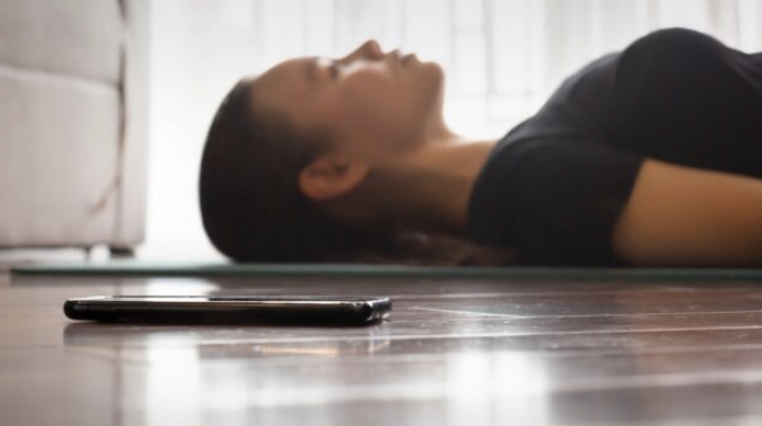 Someone lays on the ground, out of focus. A phone lays beside them, in focus.