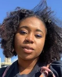 A photo of Rianna Walcott, a Black woman with curly hair blowing in the wind, blue eyeliner