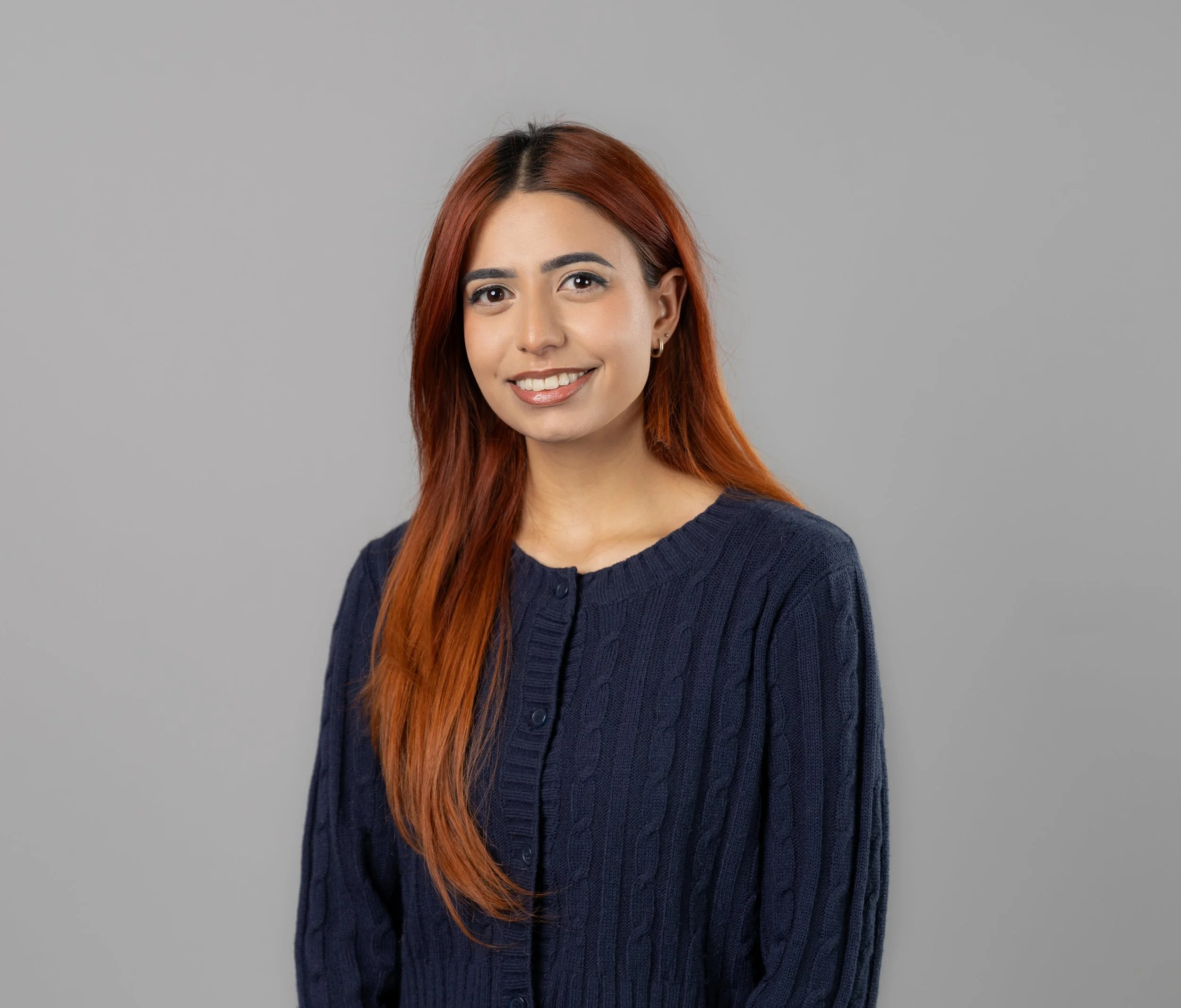 Photo of Denise Dilbir Kaur Tour, a South Asian woman with long orange hair wearing a blue sweater
