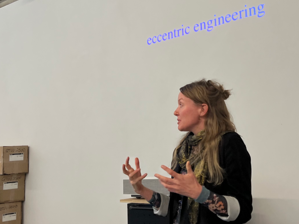 A photo of Tega Brain giving a talk, with "eccentric engineering" projected on the wall behind
