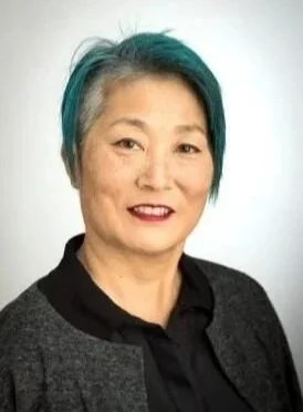 A photo of Lisa Nakamura, a woman with short gray hair, dark lipstick, and a black and gray shirt