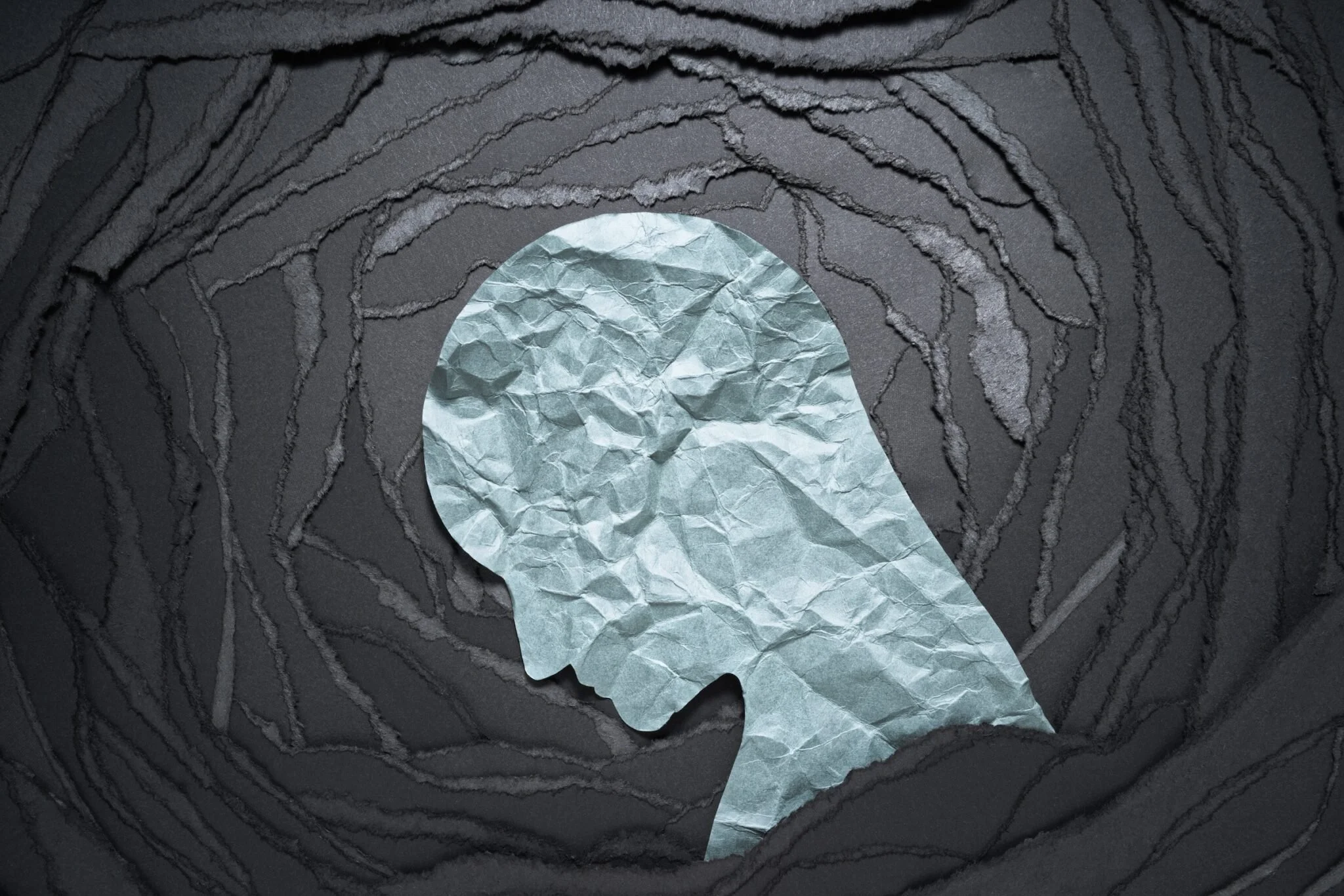 A crumpled up white piece of paper in the shape of a side profile head, surrounded by circles of ripped gray paper