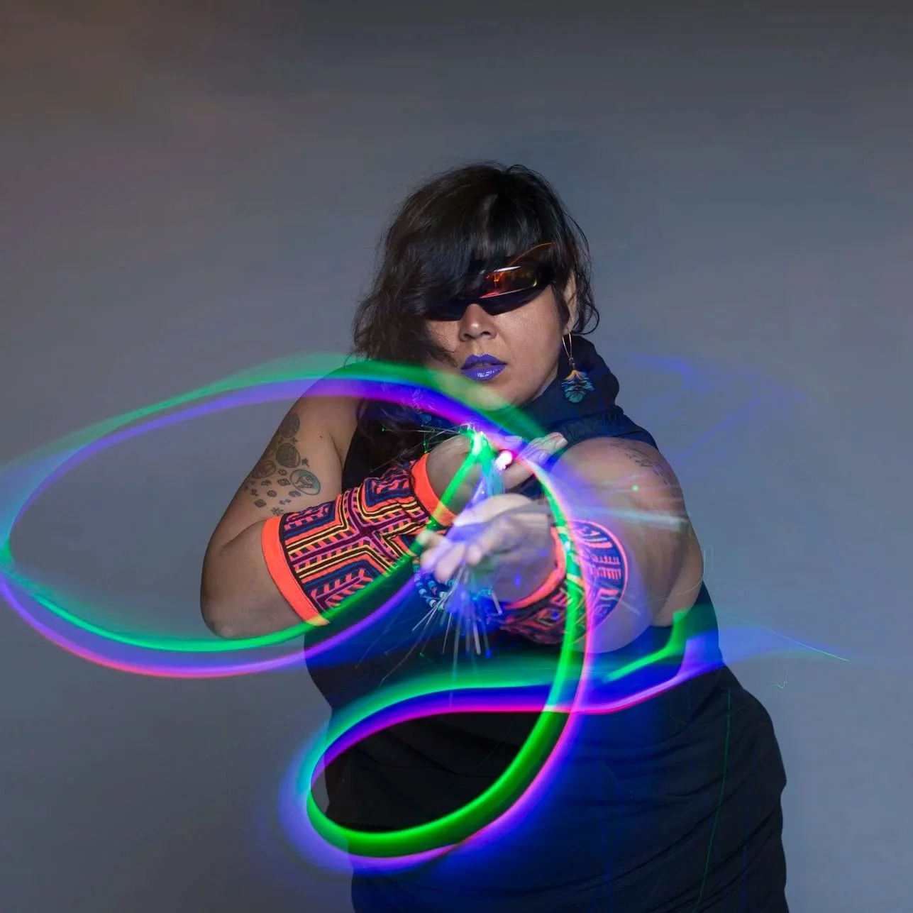 Mother Cyborg has sunglasses, tattoos, an all black outfit, and glowsticks that have transformed into lines of light thanks to long term exposure photography