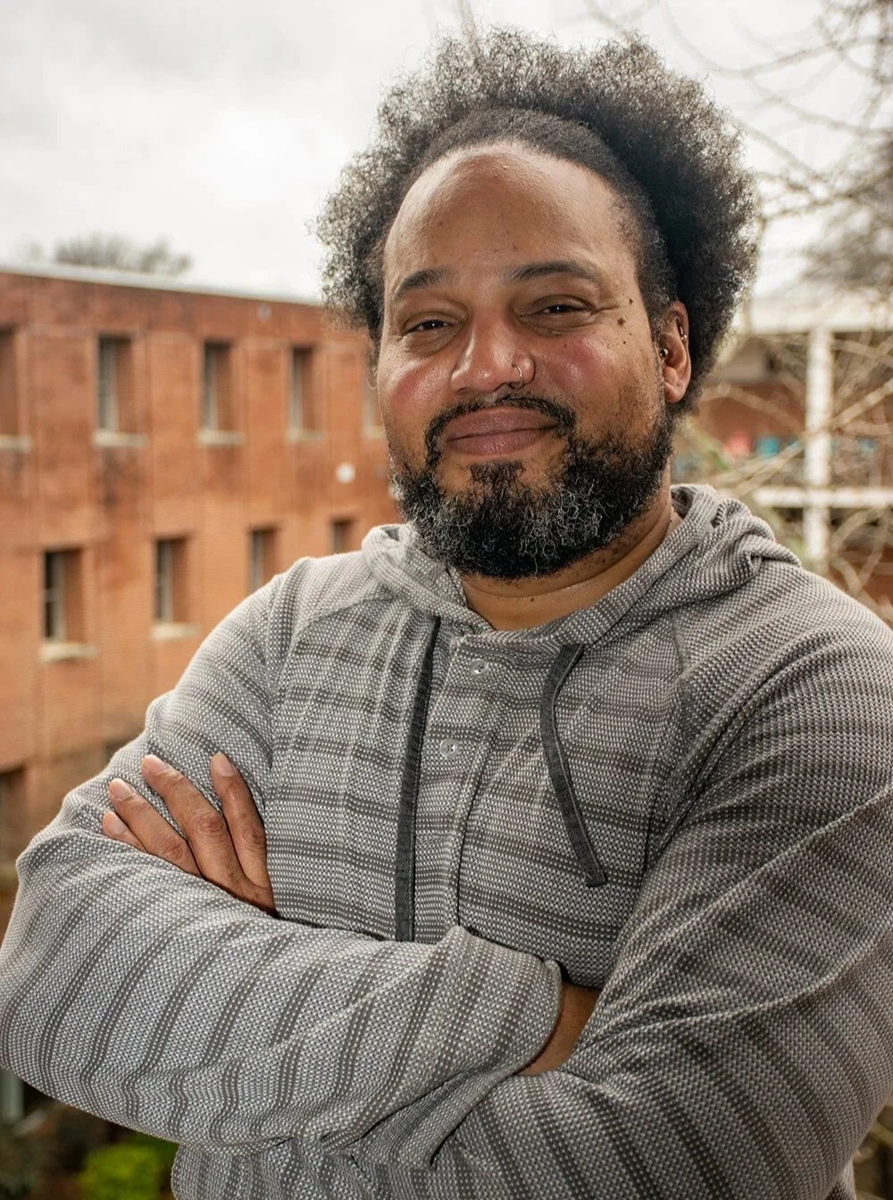 A photo of Andre Brock, a Black man with curly hair, facial hair, and a gray hoodie outdoors
