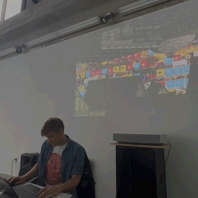 A photo of Peter Burr giving a talk, with a projection of shapes on the wall behind him