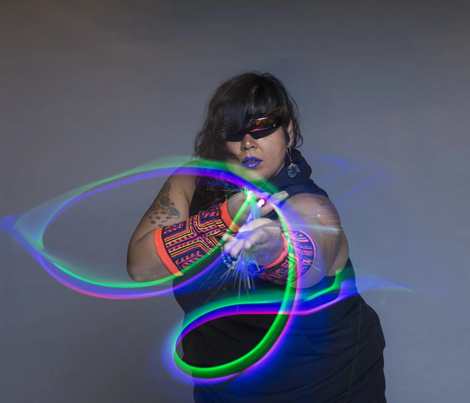 Mother Cyborg has sunglasses, tattoos, an all black outfit, and glowsticks that have transformed into lines of light thanks to long term exposure photography