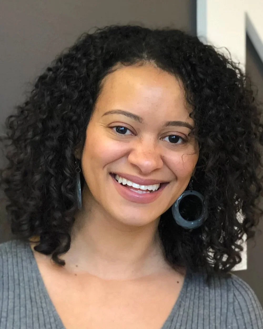 A photo of Catherine Knight Steele, a woman with dark curly hair, large hoop earrings, and a smile