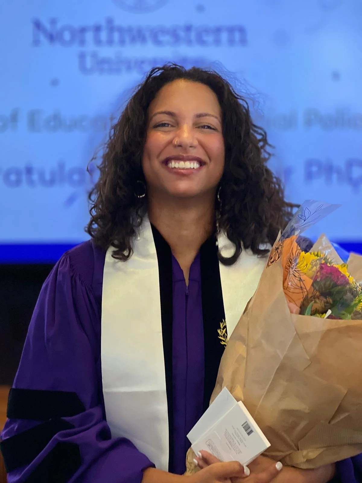 Photo of Natalie Araujo Melo, a woman with brown skin and wavy hair, at a graduation ceremony.