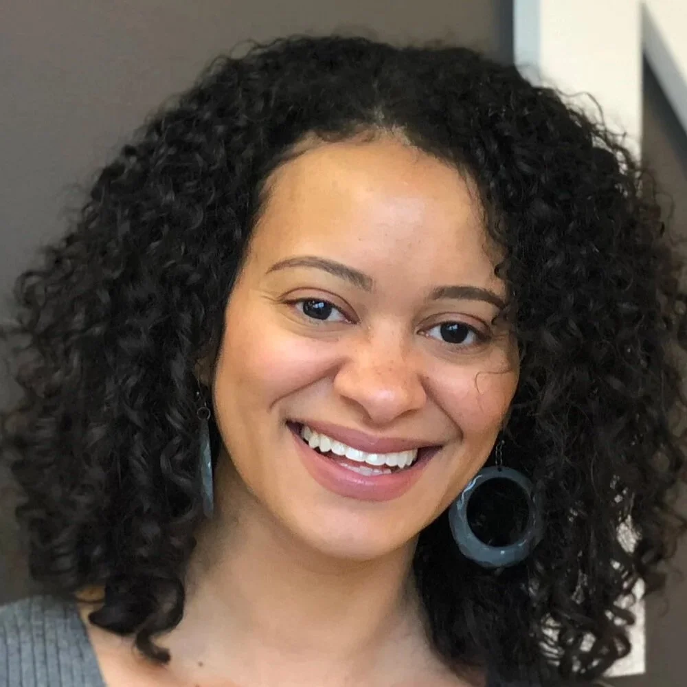 A photo of Catherine Knight Steele, a Black woman with curly shoulder length hair, a smile, and large hoop earrings