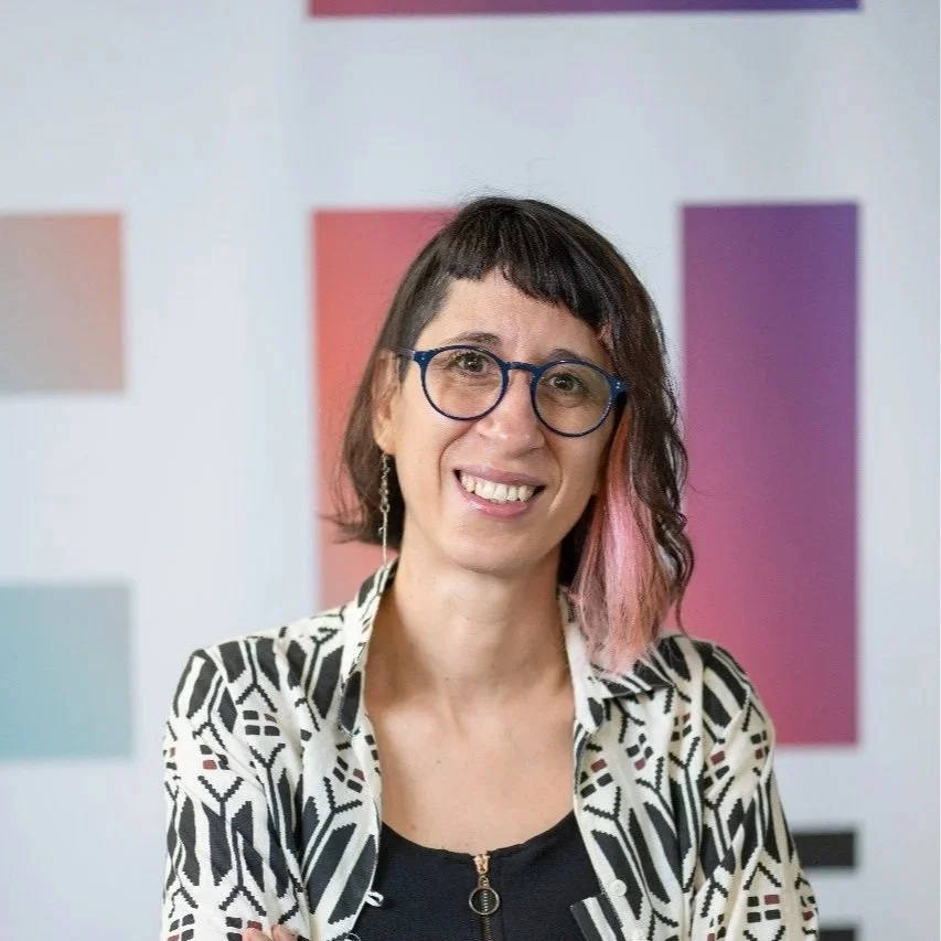 A photo of Yesica Duarte, a white individual with brown and pink hair wearing glasses and a patterned shirt