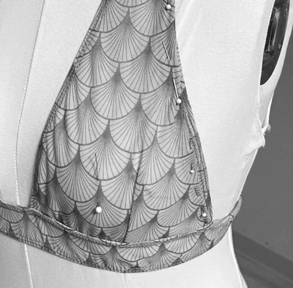 a swimwear top on a dress form with pins indicating notes for pattern adjustment