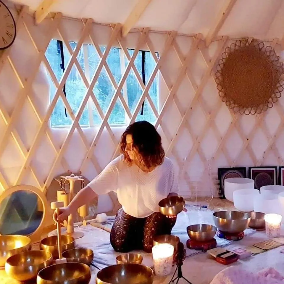 Une personne dans une structure en bois avec des bols chantants et des bougies, probablement durant une séance de méditation ou de relaxation.