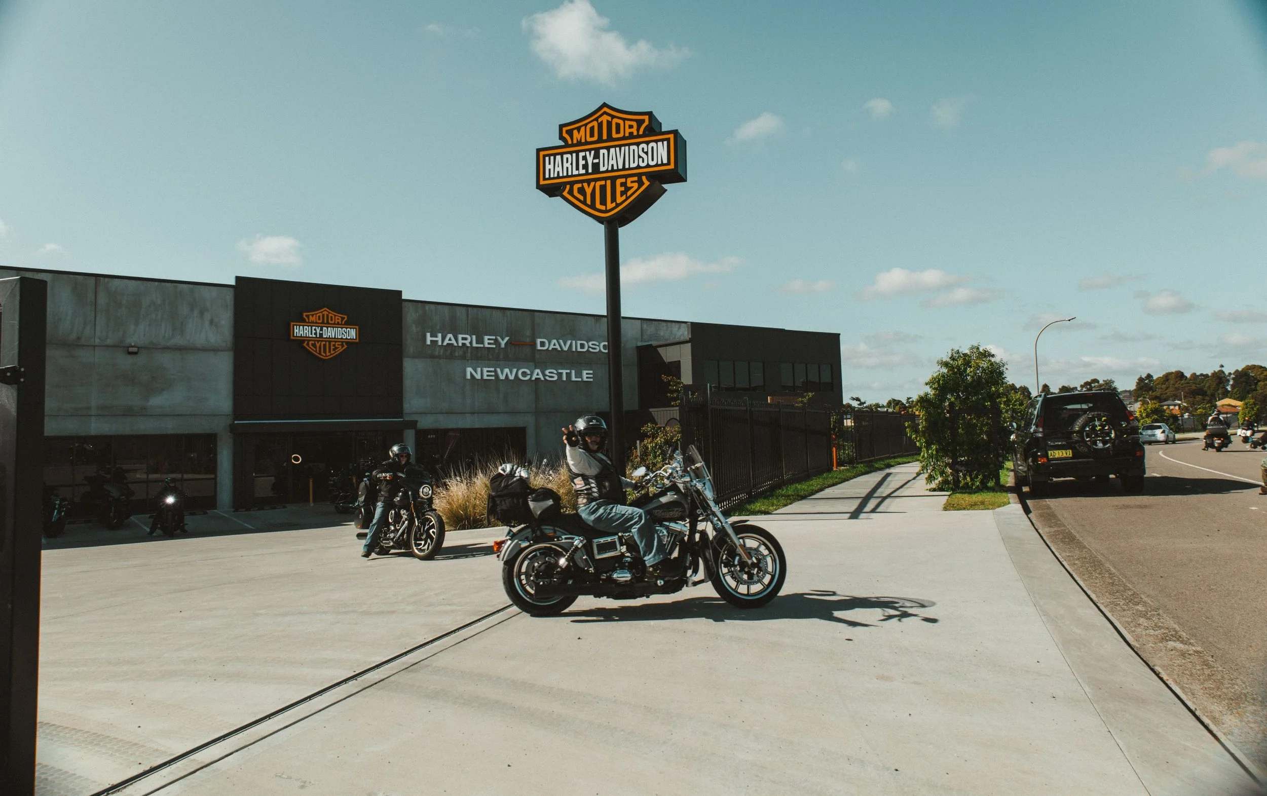Harley-Davidson dealership with motorcycles parked outside and a person riding a motorcycle in front, under a large sign.