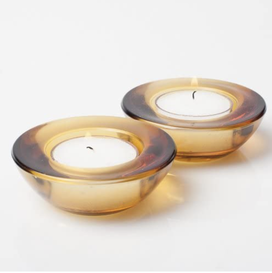 Two amber-colored glass tealight candle holders with unlit white candles inside, placed on a white surface.