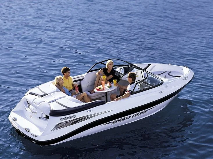A group of five people enjoying drinks and snacks on a white speedboat on the water.