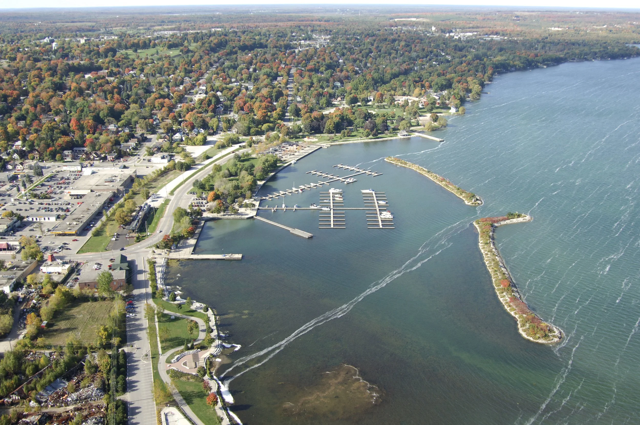 An aerial view of a Orillia, Ontario harbor with docks and boats, surrounded by a residential area with trees in fall colors and a parking lot.