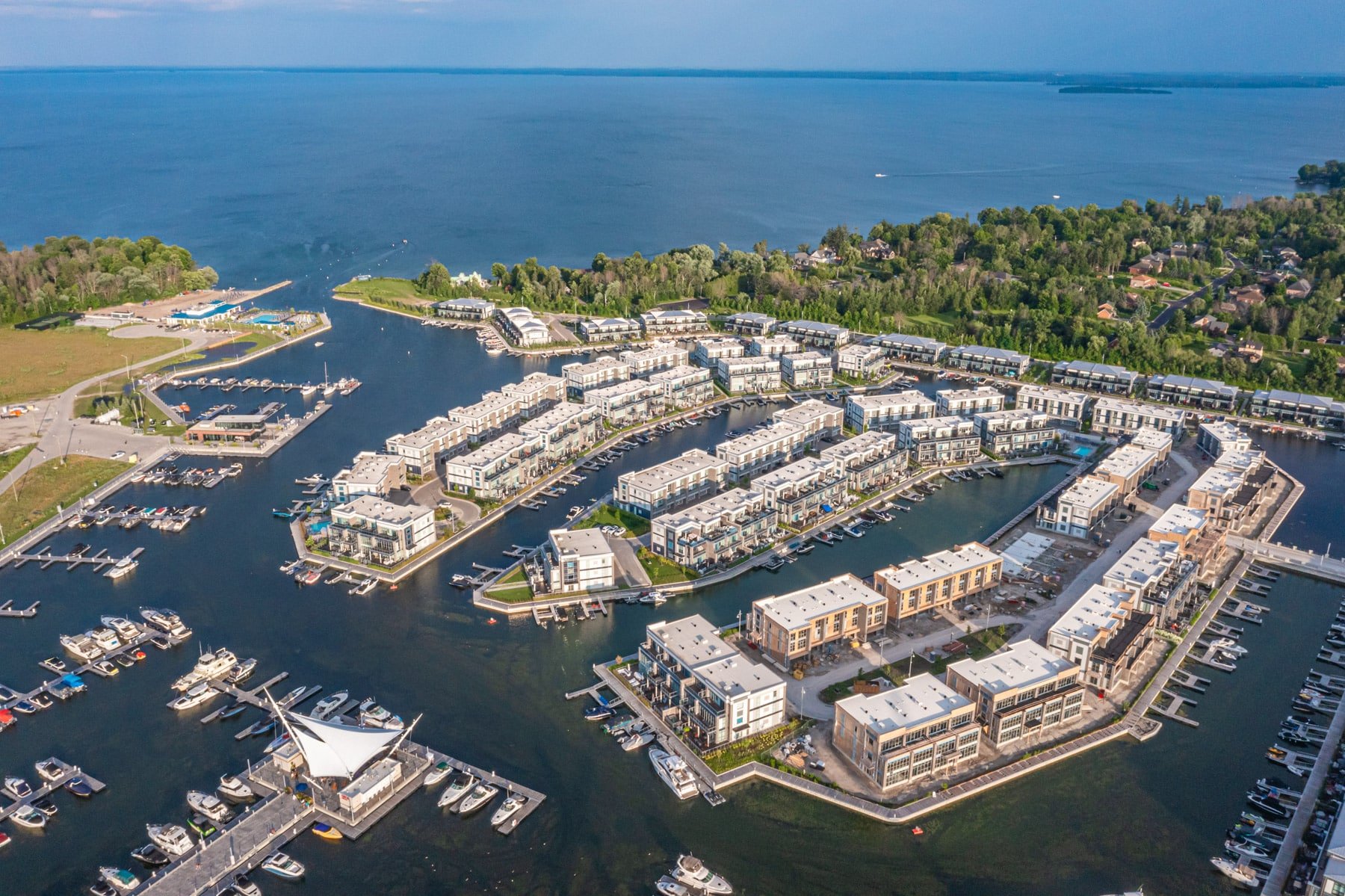 Aerial view of a Friday Harbour Resort with modern residential buildings and boats docked in the water, with a large body of water and green landscape in the background.