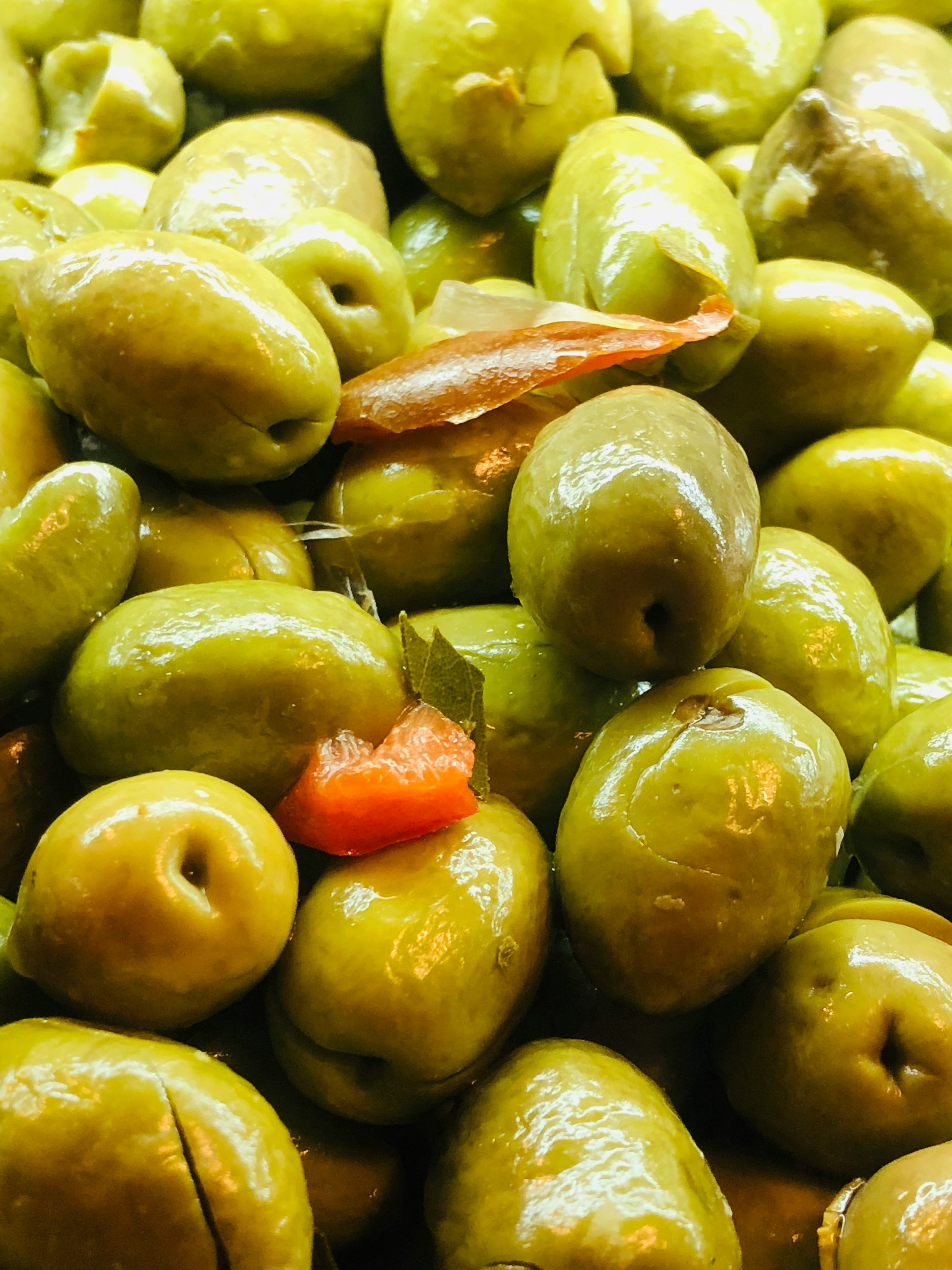 Close-up of green olives with a few pieces of red pepper and bay leaves.