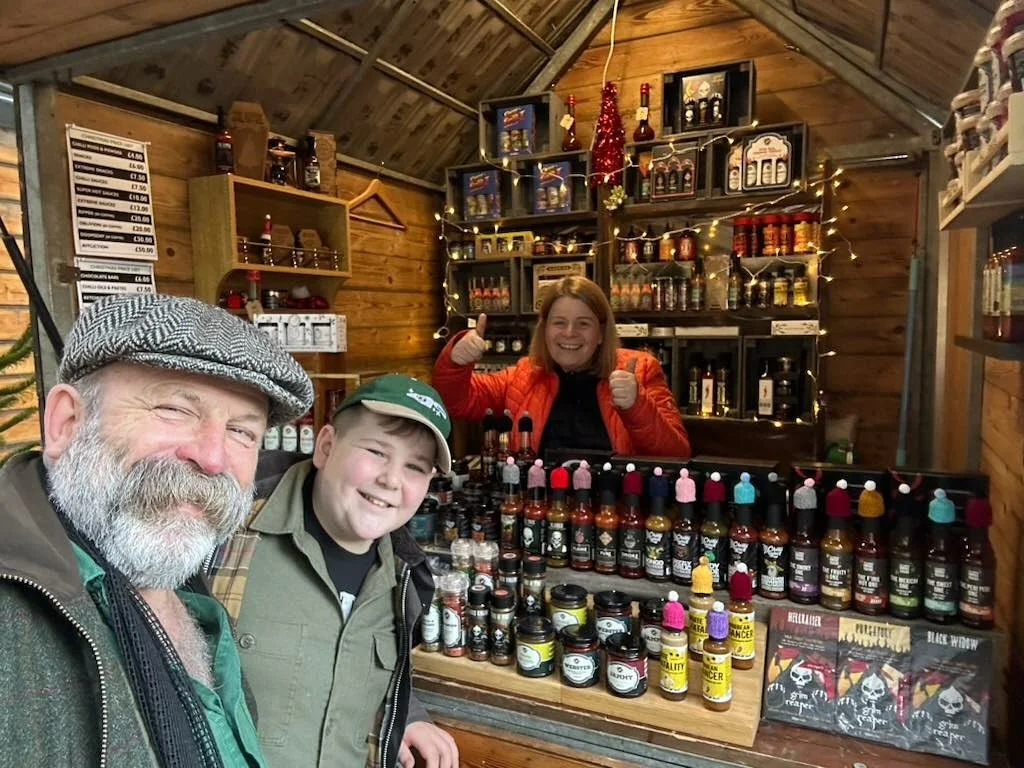 Three people smiling at a spice stand inside a wooden store with shelves of spices, sauces, and decorative items.