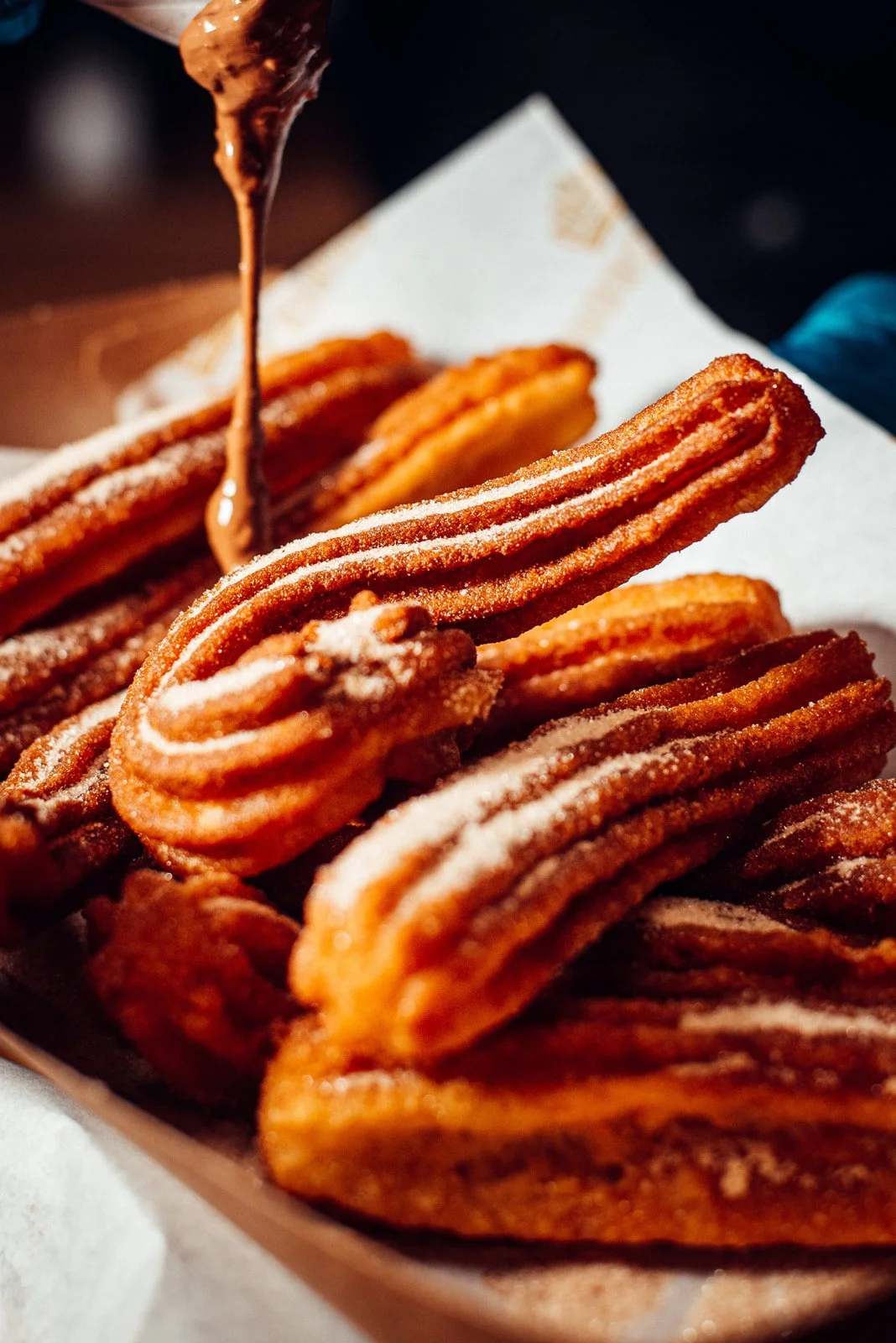 Close-up of churros coated with cinnamon sugar, with chocolate sauce being poured over them.