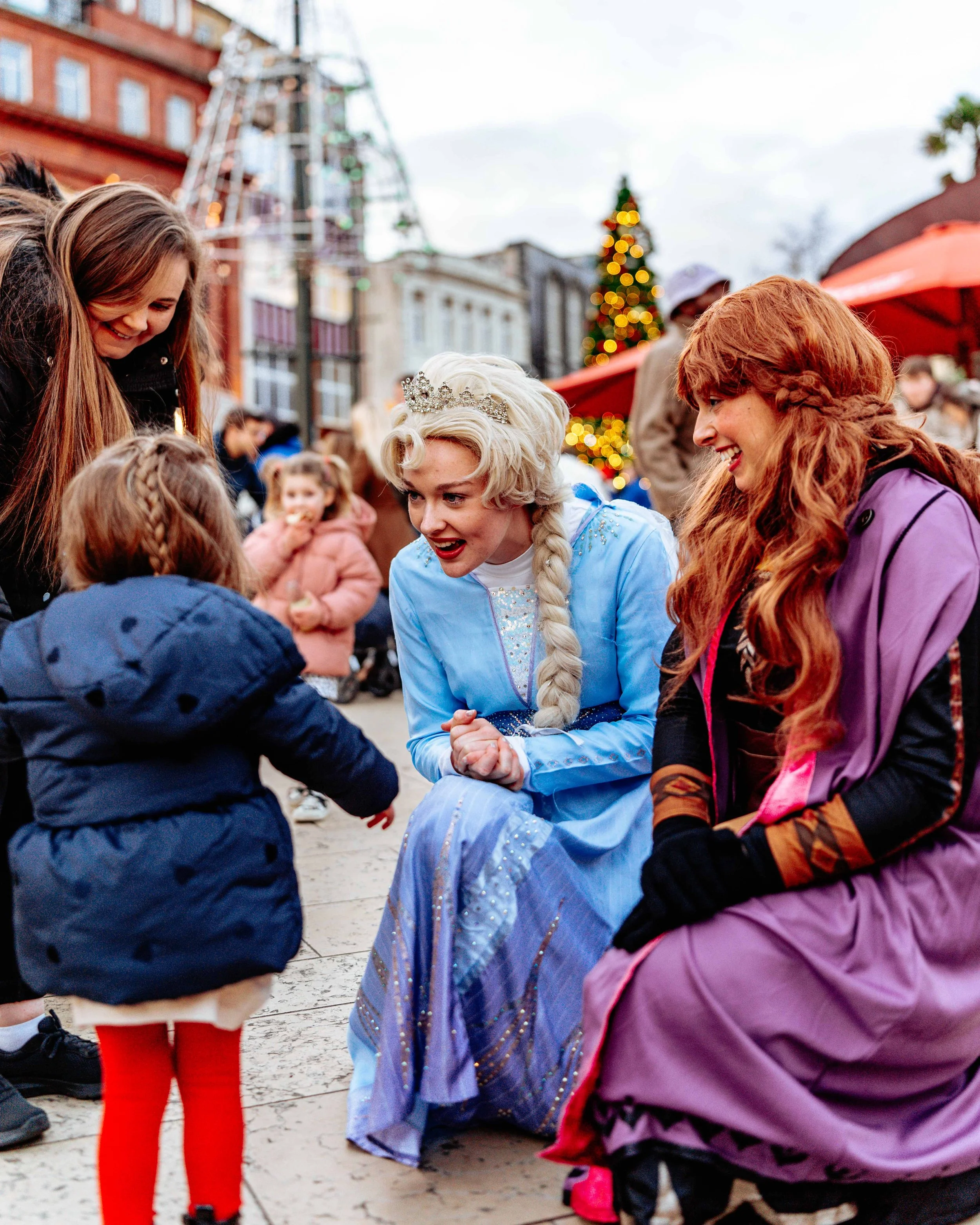 Children meeting Disney's Elsa at a festive outdoor event with Christmas decorations in the background.