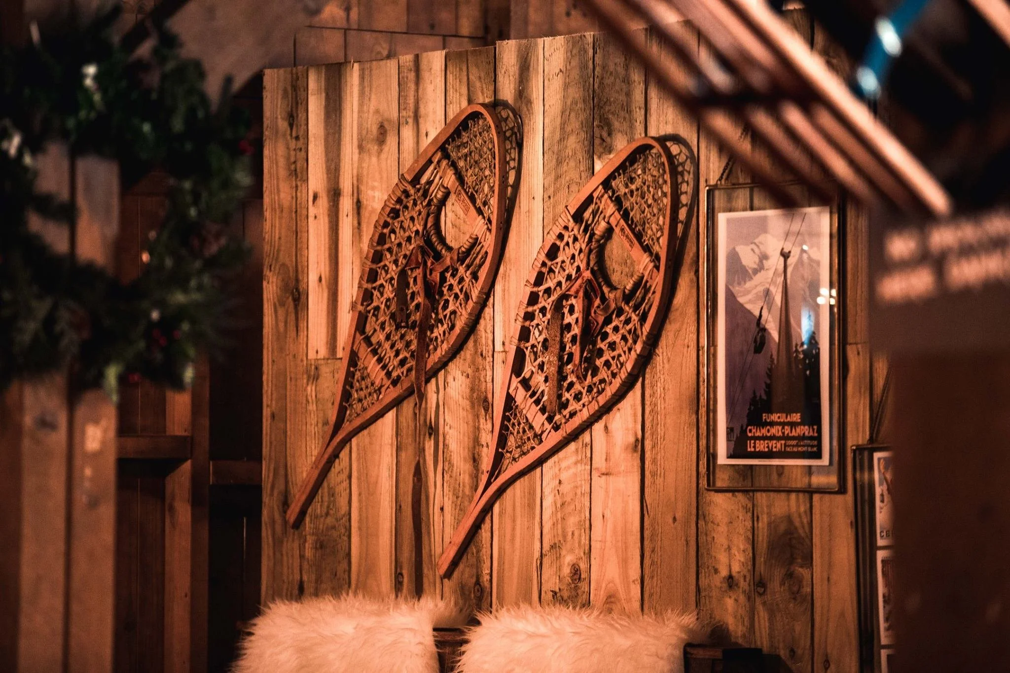 Decorative snowshoes mounted on a wooden wall in a cozy, rustic setting, with framed artwork and fluffy chairs below.