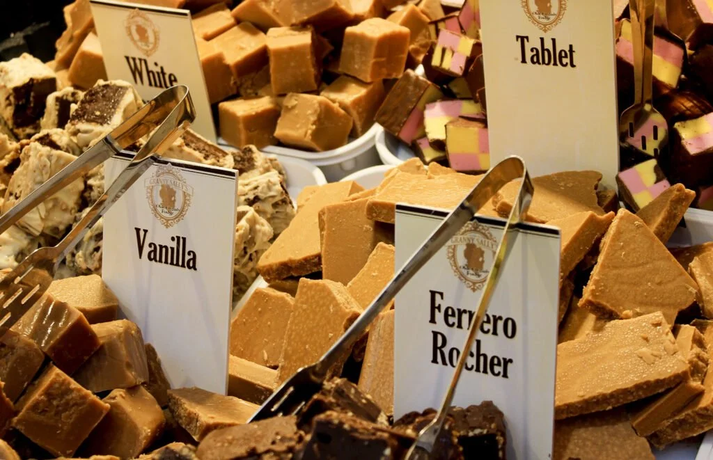 Assorted types of fudge at a candy shop with labels for vanilla, Ferrero Rocher, white, and tablet.