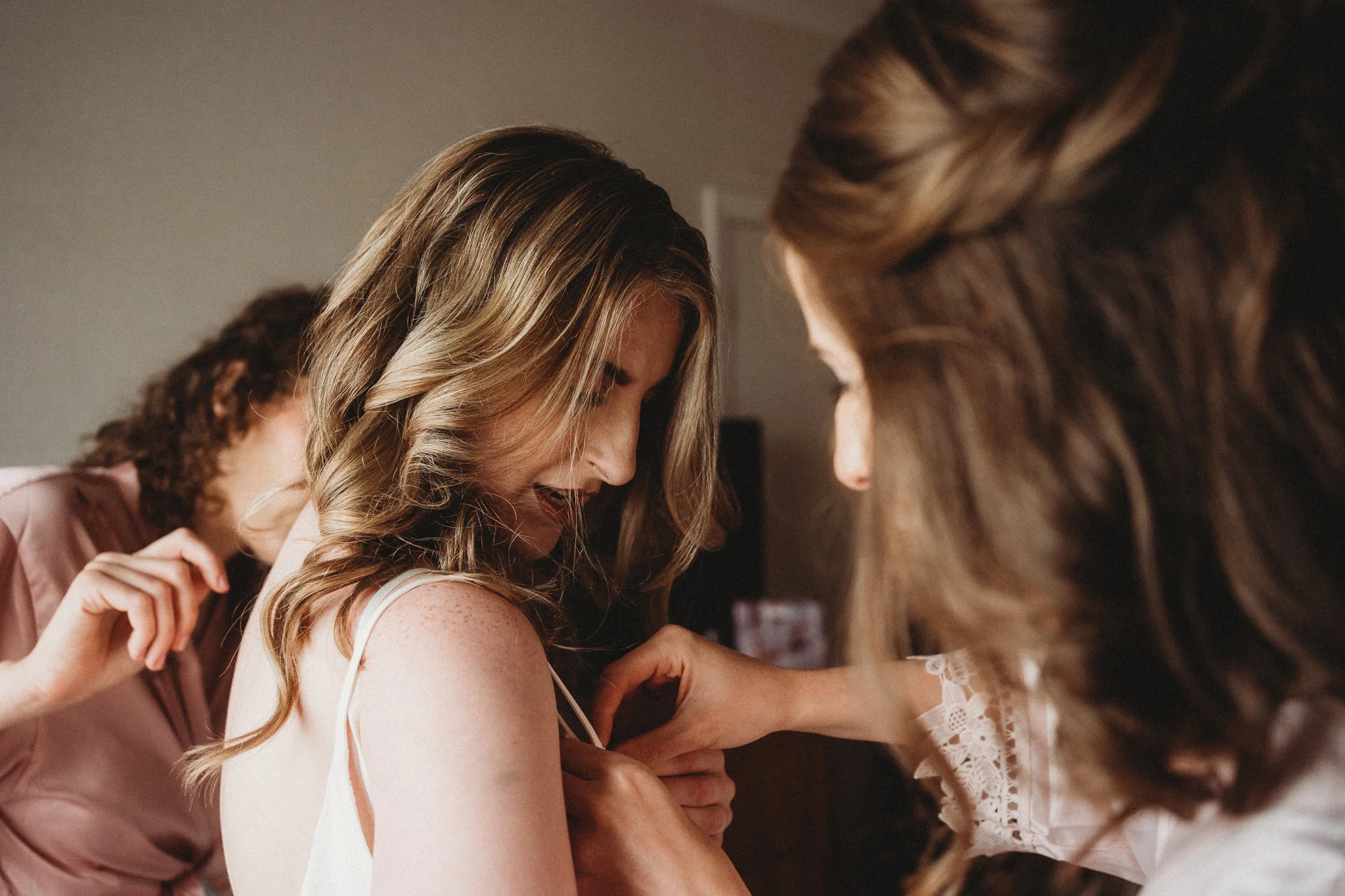 Bride preparing for her wedding day with bridesmaids adjusting the dress - documentary/reportage style wedding photography