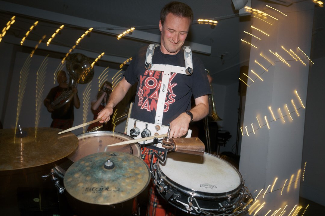  The New York Brass Band's drummer smiling as he plays, with streaks of light around him, at The Tetley in Leeds. 