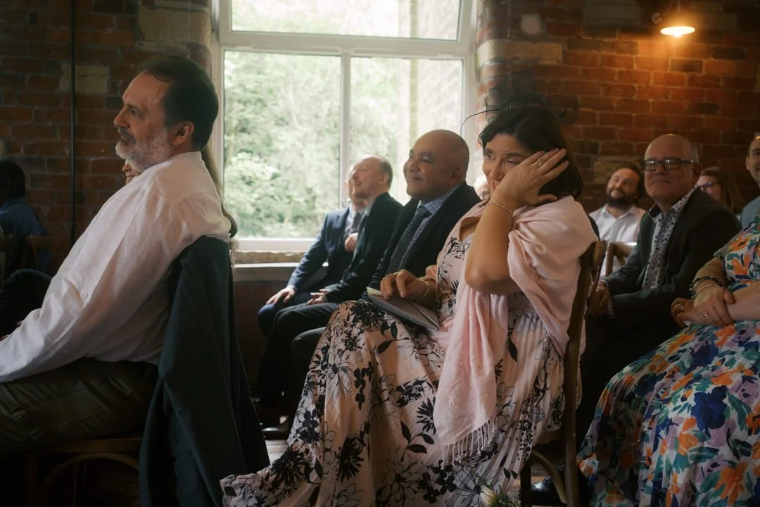  A guest laughing with her hand to her face during the ceremony 