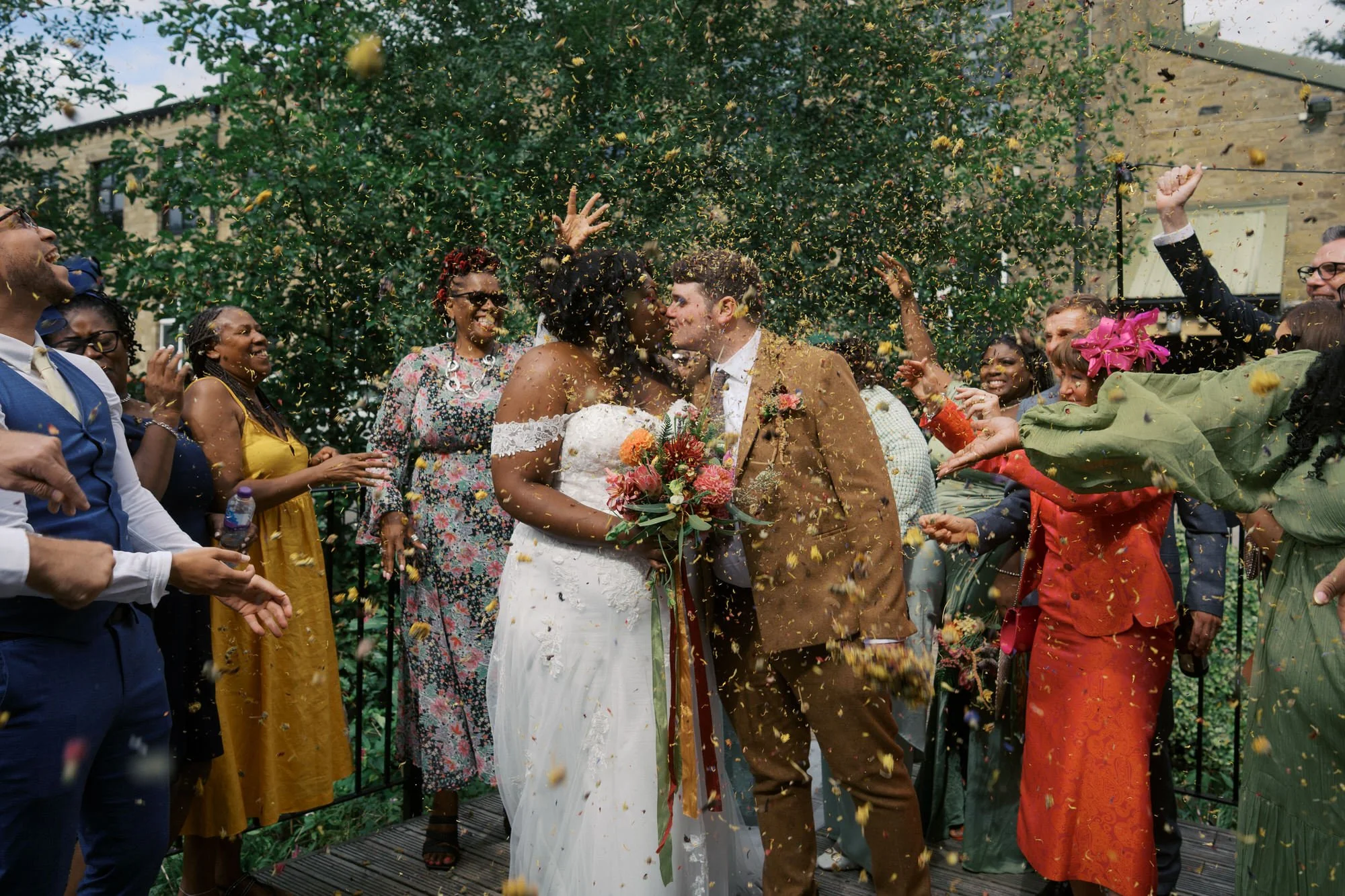  Guests throwing confetti over the bride and groom as they kiss at Bowers Mill 