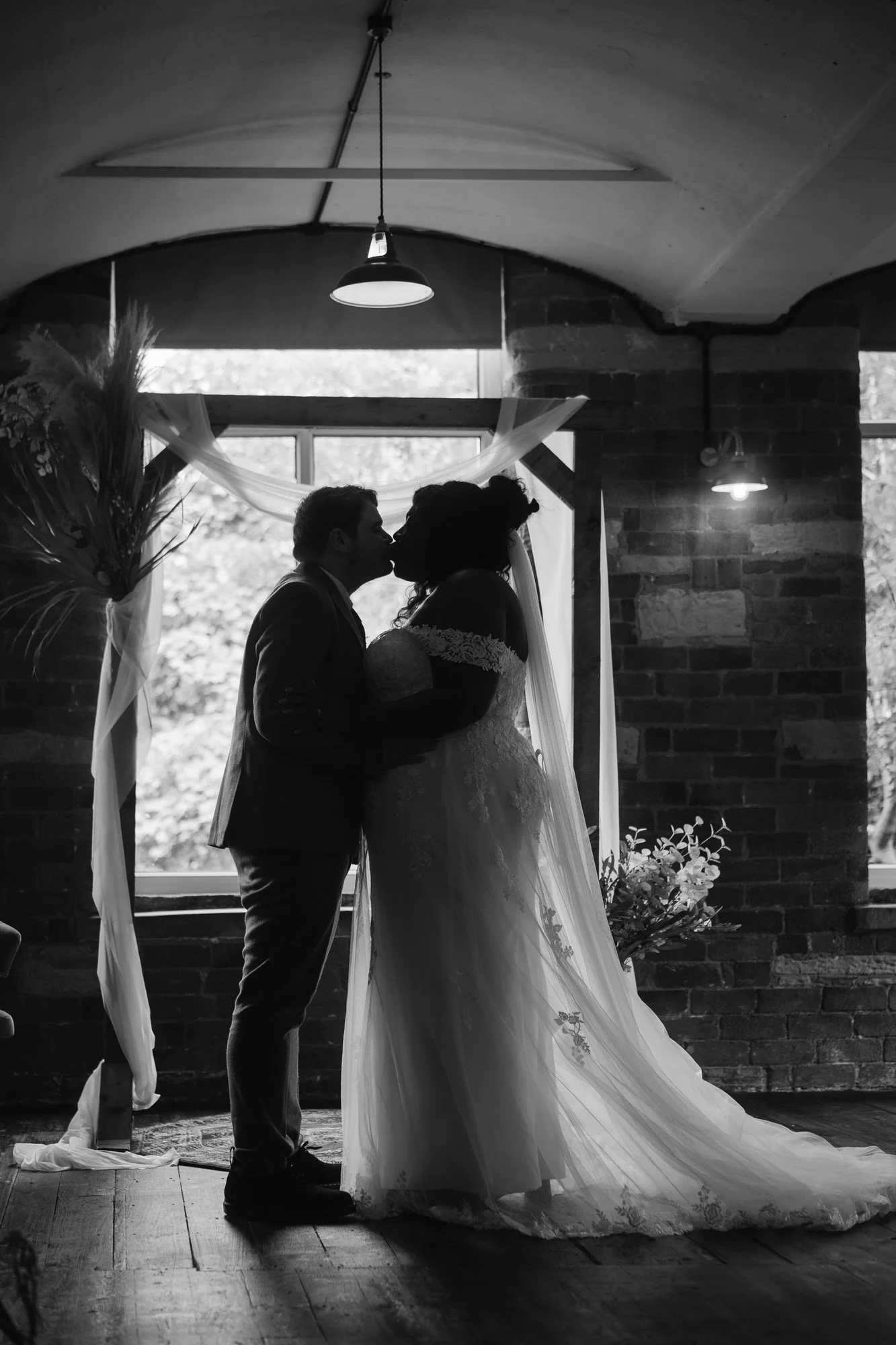  Black and white silhouette of the bride and groom kissing under the wedding ceremony arch at Bowers Mill 