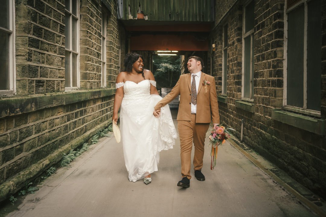  The bride and groom laughing as they walk through a stone passage at Bowers Mill 