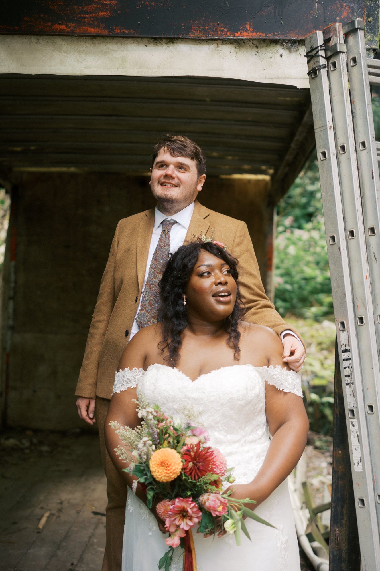  The groom standing behind the bride under an old rusted canopy at Bowers Mill 