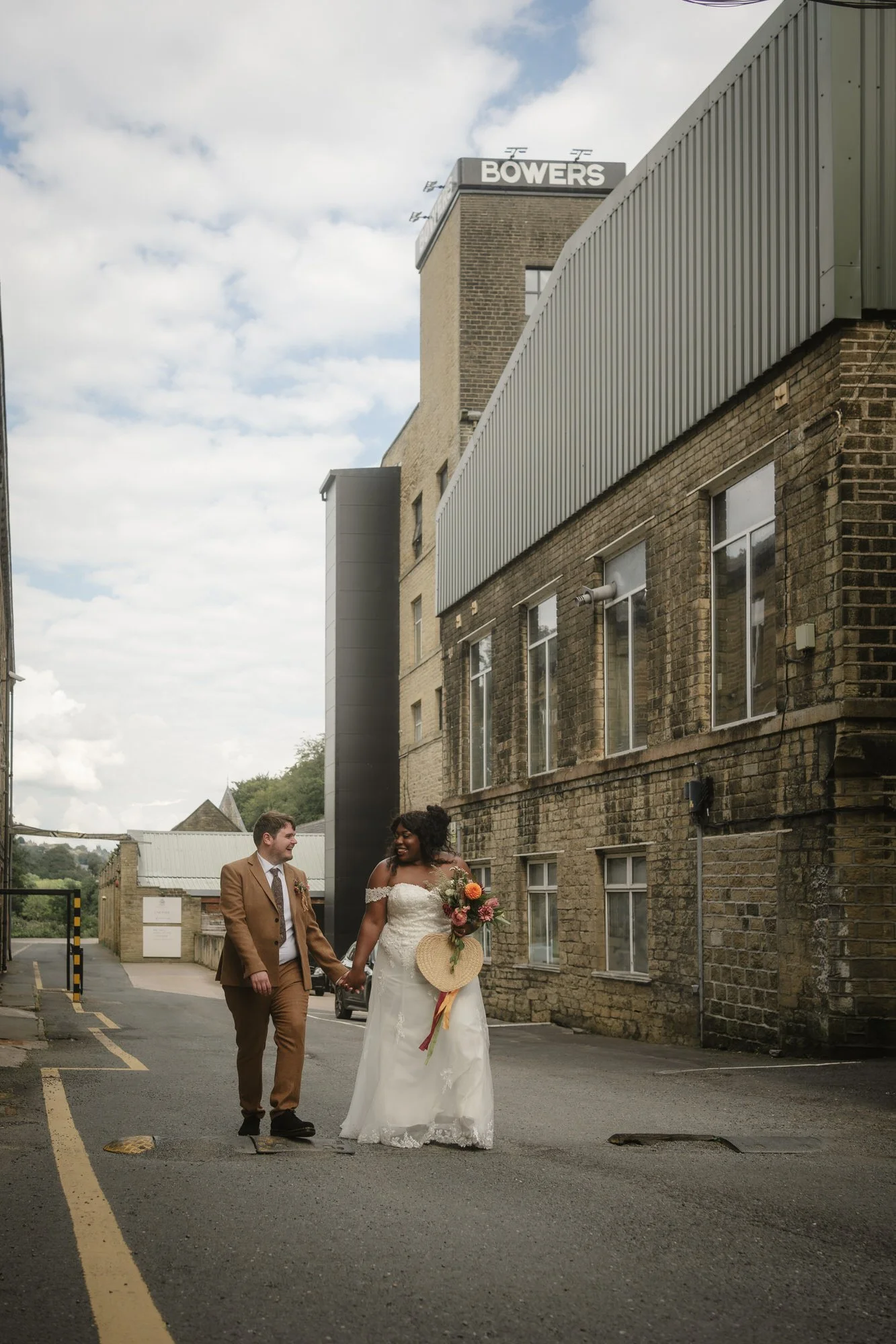  The bride and groom walking hand in hand beneath the Bowers tower, near Halifax 