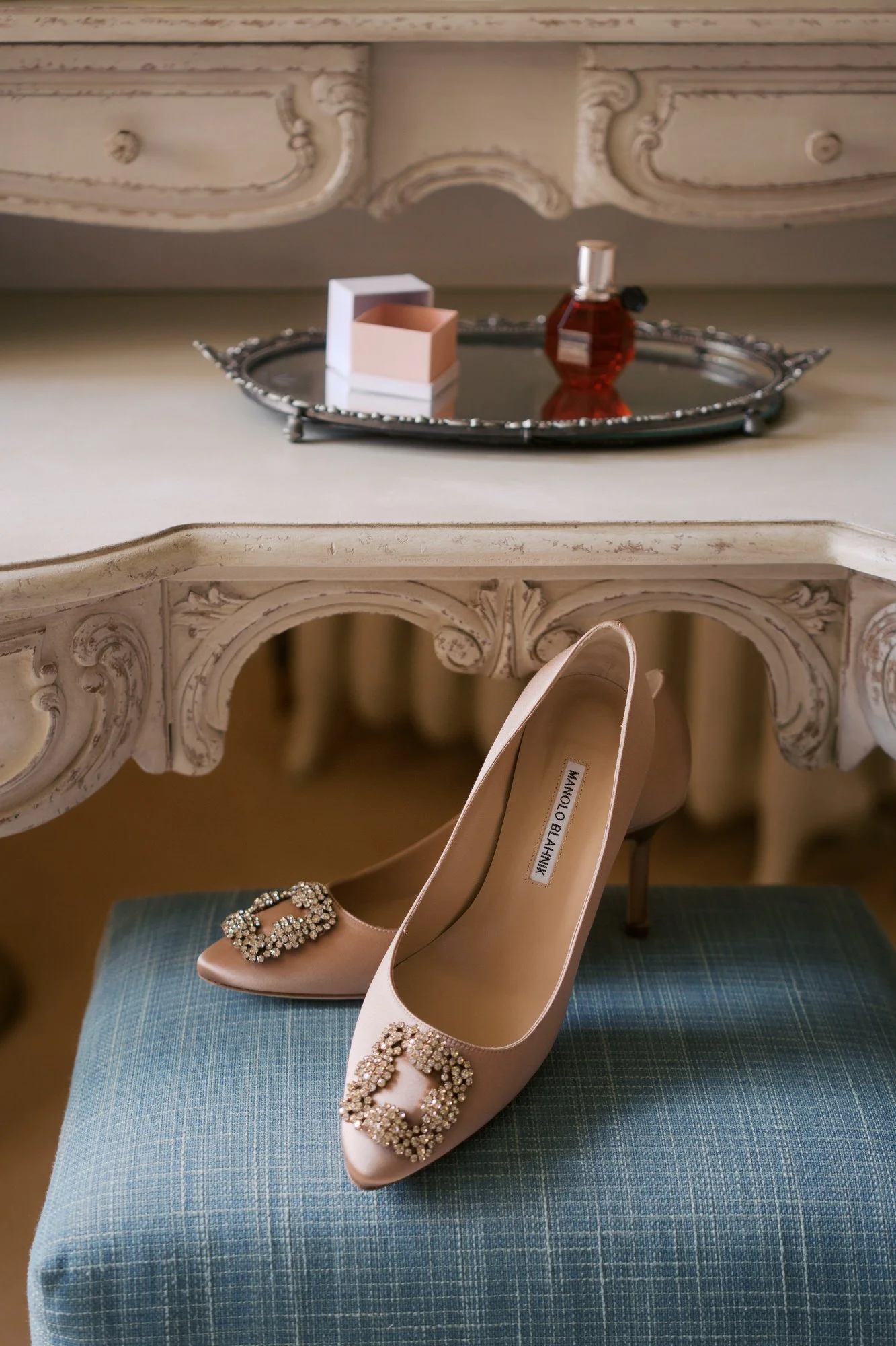  Blush bridal shoes on a blue upholstered stool beneath an ornate white dressing table 